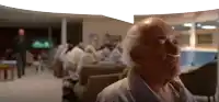 an elderly man wearing an oxygen mask is sitting in a room with other people