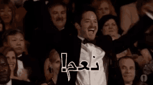 a man in a tuxedo is covering his mouth with his hands while sitting in a crowd of people .