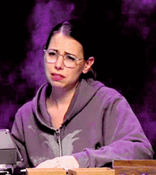 a woman wearing glasses and a purple sweatshirt is sitting at a desk