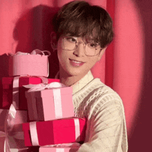 a young man wearing glasses holds a stack of pink gifts