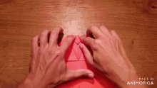 a person 's hands folding a piece of red paper with the words made in animotica below them