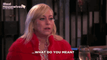 a woman is sitting at a table with a glass of wine and says " what do you mean "