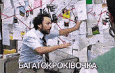 a man in a blue shirt and tie is pointing at a bulletin board with a lot of papers on it ..