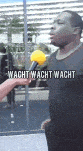 a man is being interviewed with a yellow microphone and the words wacht wacht wacht are visible