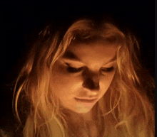 a close up of a woman 's face in the dark with a candle shining on her face .