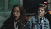a boy and a girl are sitting next to each other with a trt 1 logo in the background