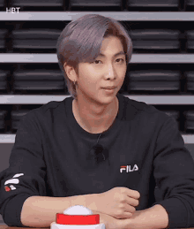 a young man with purple hair is wearing a black fila sweatshirt