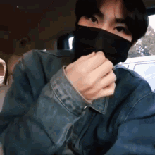 a man wearing a mask and a denim jacket is in a car .