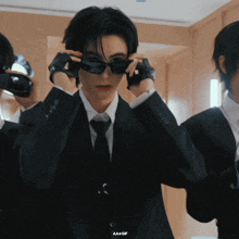 a man in a suit and tie adjusts his sunglasses with a gif below him