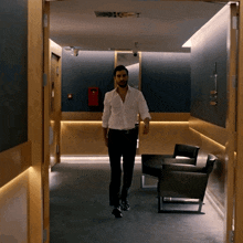 a man walking down a hallway with a fire extinguisher on the wall