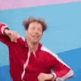 a man in a red jacket is dancing in front of a pink and blue wall .