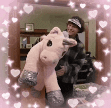 a person holding a pink stuffed unicorn with hearts around it