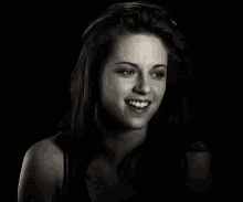 a black and white photo of a woman smiling in a dark room .