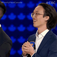 a man in a suit and glasses is smiling in front of a microphone with the words family feud canada above him