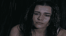 a woman with wet hair looks at the camera while standing in the rain