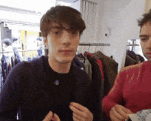 a man in a black shirt with a blue circle on it is standing next to another man in a red shirt in a clothing store
