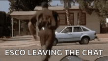 a man is running down a street in front of a house with a car in the background .