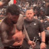 a shirtless man is being escorted by a bearded man in a black shirt