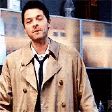 a man in a trench coat and tie is standing in front of a counter .
