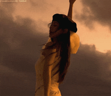 a woman in a white dress and a black hat is dancing in front of a cloudy sky