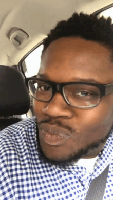 a man wearing glasses and a plaid shirt is sitting in the back seat of a car