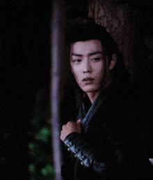 a young man in a black outfit is leaning against a tree in the dark