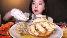 a woman in white gloves is eating a large crab on a white plate .
