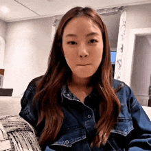 a woman in a denim jacket is sitting on a couch making a face
