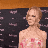 a woman in a pink dress is standing in front of a wall with the word babygirl written on it .