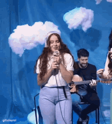 a woman is singing into a microphone while a man plays a guitar in the background .