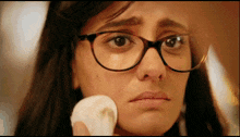 a woman with glasses is cleaning her face with a cotton pad