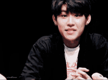 a young man in a black jacket is smiling and making a peace sign with his fingers