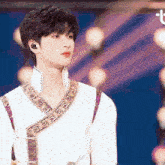 a man wearing a white shirt with a purple and gold embroidery