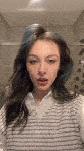 a woman with blue hair is wearing a white sweater vest
