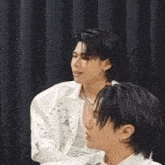 two men are sitting next to each other and one is covering his mouth with his hands .