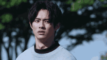 a young man wearing a gray shirt and black collar looks at the camera