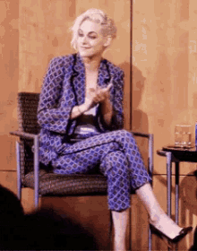 a woman in a blue suit is sitting in a chair and clapping her hands .