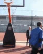 a man in a blue jacket is standing in front of a basketball hoop .