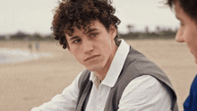 a man with curly hair looks at the camera while another man looks on