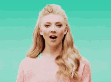 a woman in a pink sweater is standing in front of a blue background .