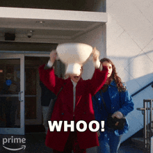 a woman in a red coat is throwing a pillow in the air and the word whoo is on the bottom right