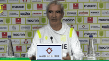 a man stands at a podium in front of a wall with logos for macron