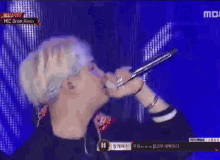 a man singing into a microphone on a stage with the words mic drop remix on the screen behind him