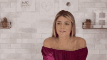 a woman in a pink off the shoulder top stands in front of a brick wall with a sign that says nao desista