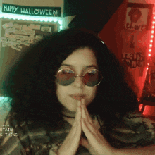 a woman wearing sunglasses is sitting in front of a sign that says happy halloween