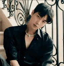 a young man in a black shirt and necklace is sitting on a set of stairs .