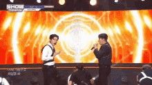 two men are standing on a stage holding microphones and dancing .