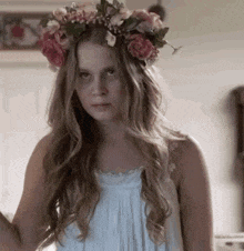 a woman wearing a flower crown and a white dress is making a funny face .