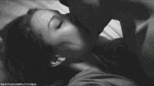 a black and white photo of a man and woman kissing in bed .