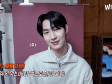 a young man in a white sweater is smiling in front of a pink background with chinese writing